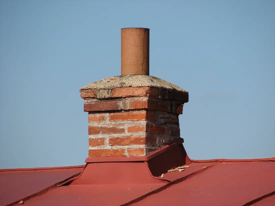 Brick chimney with a clay flue pipe and metal flashing where it meets a red metal roof
